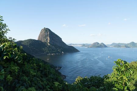 View from the mountain top Forte Duque de Caxias in Leme, Copacabana, overlooking the rock Sugarloaf Mountain in Rio de Janeiro. There is blue sky and sea, green tropical forest, blue sea coastline.の写真素材