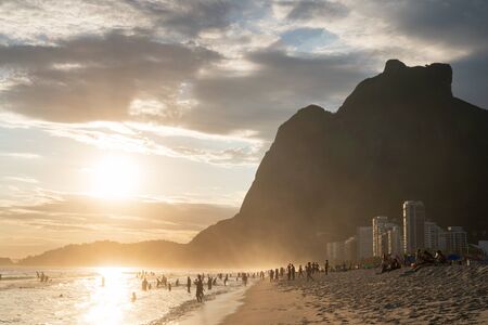 Rio de Janeiro, Brazil - January 7, 2020: Sunset from Sao Conrado Beach, with the tall seaside granite mountain Pedra da Gavea. Golden light shines on the white sand and sea, with clouds in the sky.のeditorial素材