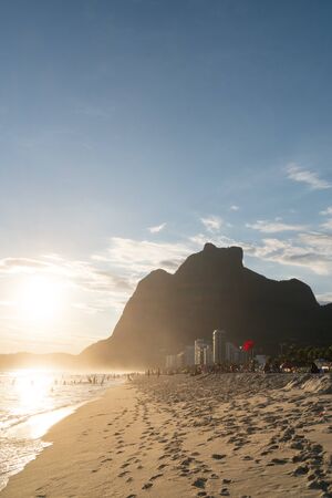 Rio de Janeiro, Brazil - January 7, 2020: Sunset from Sao Conrado Beach in Rio de Janeiro, with the tall seaside granite mountain Pedra da Gavea. There is blue sky, white sand and golden light.のeditorial素材