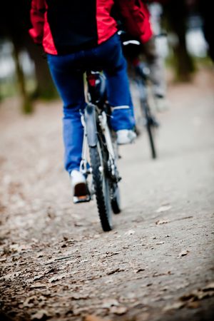 Two bicyclists going on a wood track - front focus