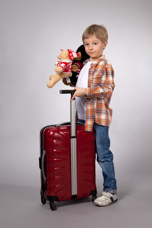Boy with red suitcase with toys and going on the roadの写真素材