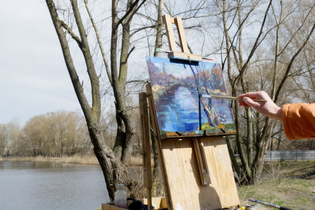 Artist draws a brush and oil paints spring landscape with a lake and treesの写真素材