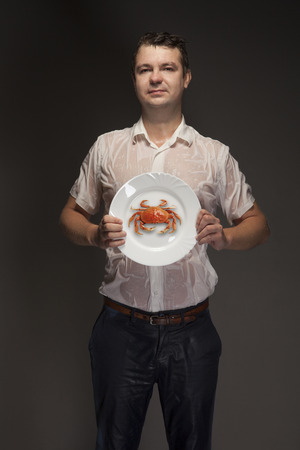 Portrait of a wet young man with a crab on a plateの写真素材
