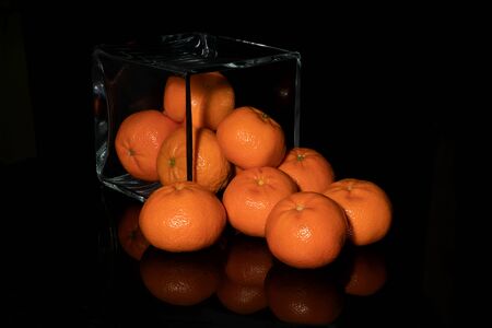 Tangerines sprinkled from a glass cube on a black backgroundの写真素材
