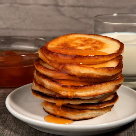 Several pancakes, glass of milk and apricot jam on wood background.
