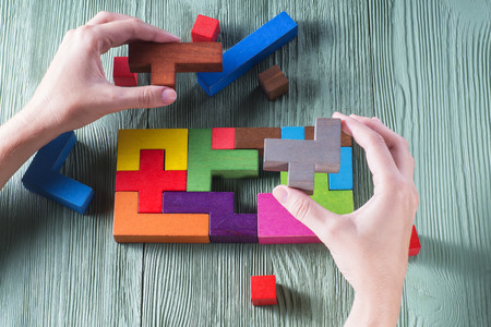 Hand holding wooden puzzle element. Hand sets the last element of the puzzle. The concept of logical...