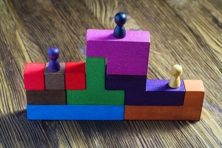 Three wooden toy figures on the podium. Persons standing on the podium.