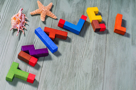 Travel Word of colorful wooden puzzles on a wooden background with shells and starfish.