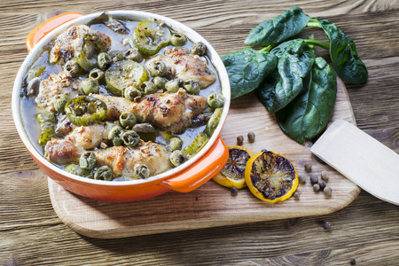 Baked chicken drumsticks in orange dish. Chicken cooked with green olives and pickles. Roasted Chicken Legs on a rustic wooden background with copy space.の写真素材