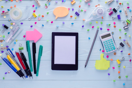 Office, business, education still life concept on blue wooden background. Top view of wooden desktop with e-book and bright colorful stationery items. Set of mock up e-book and stationery, flat lay.の写真素材