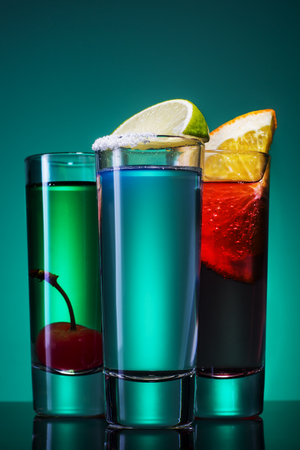 Shooters  drinks. Three short cocktail on a blue background, concept for drinks offers at promotional evenings. Cocktails with lime, orange, cherry.の写真素材