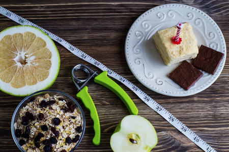 Concept of making choice of food: fruit, oatmeal and sports or cake and candy, separated by a measuring tape. Time for slimming.の写真素材