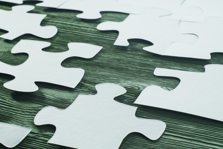 The concept of logical thinking. Logical conundrum. White jigsaw puzzle on a wooden background. Business concept with white jigsaw puzzle on green wooden background. Placing missing a piece of puzzle.の写真素材