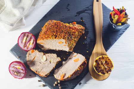Roast pork with with mustard, onions. pepper and lemon on a white wooden table, top view. Baked meat on a black slate board, flat lay.の写真素材