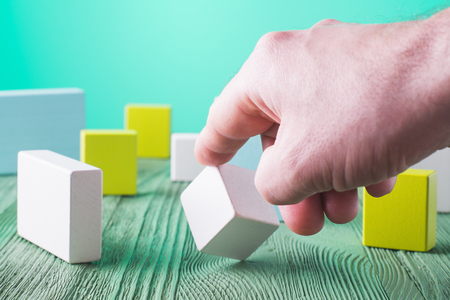 Hand holding wooden cube element. The concept of logical thinking. Geometric shapes on a wooden background. Man's hand holding wooden block. Colorful wooden blocks.の写真素材