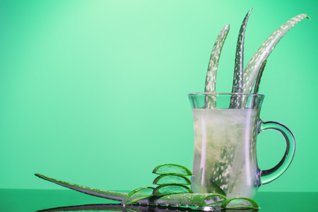 Leaves of Aloe Vera cactus in a glass. Aloe vera juice in glass on green background with space for text. Healthy drink with aloe with copy space.の写真素材