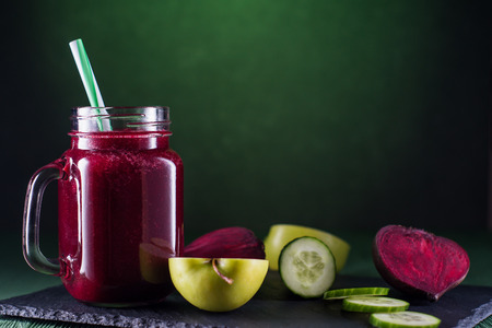 Beetroot smoothie in a mason jar with a straw and ingredients on a wooden background. Fresh beet juice, detox. Organic antioxidant smoothies made of beet, apple, cucumber. Healthy vegan raw food.の写真素材