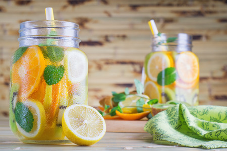 Detox fruit water on wooden table. Fresh homemade lemonade with mint. Summer refreshing citrus water in a mason jar on a bamboo table. Summer homemade cocktail with lemon, orange, kiwi.の写真素材