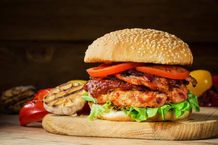 Fresh tasty burger. Hamburger close-up, sesame buns with succulent beef patty, grilled onions, bacon, tomato and fresh salad served on rustic wooden board. Homemade hamburger with fresh vegetablesの写真素材
