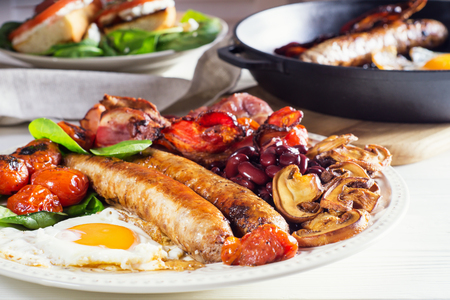Delicious full English breakfast with fried egg, bacon, sausage, tomatoes, beans and mushrooms.  Traditional english breakfast on white wooden background, close-up.の写真素材