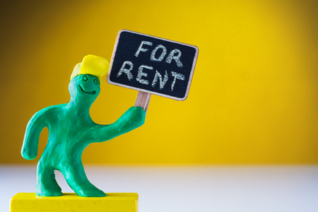 Plasticine green man holds a sign with an inscription in his hand - for Rent. Man holds a wooden tablet in his hands.の写真素材