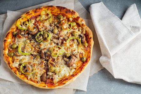 Delicious homemade pizza with tomato sauce, mushrooms, chicken, parmesan, peppers and olives on the granite table. Top view, flat lay. Tasty Italian pizza.の写真素材