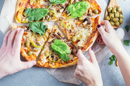Man and woman hands take a pieces of pizza sliced. Hands taking pizza cuts from table. Italian pizza with tomato sauce, mushrooms, chicken, parmesan, peppers on granite table. Top view, flat lay. の写真素材