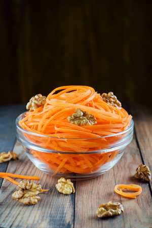 Bowl with fresh grated carrot. Organic salad with fresh carrot, walnuts and oil in glass bowl on wooden background. Healthy food, detox salad. Diet concept.の写真素材