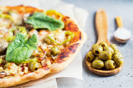 Delicious homemade pizza with tomato sauce, mushrooms, chicken, parmesan, peppers and olives on the granite table and wooden spoons with olives and salt. Tasty Italian pizza.の写真素材