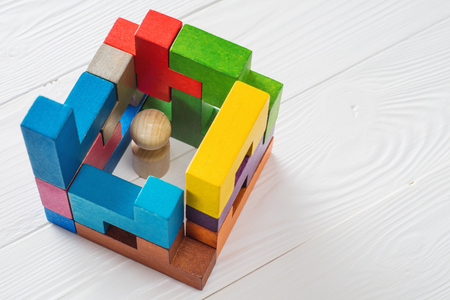 Business metaphor, businessman in a trap on white wooden background with copy space. Businessman trapped inside a abstract room from colourful wooden blocks. The concept of problems in business.の写真素材