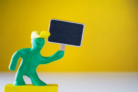 Plasticine green man holds an empty wooden sign in his hand.の写真素材