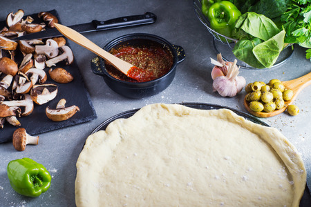Pizza preparation, raw dough surrounded by ingredients. Male hand smudging sauce on pizza dough. の写真素材