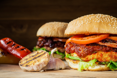 Two fresh tasty burger. Homemade hamburger with fresh vegetables, close-up. Sesame buns with succulent beef patty, grilled onions, bacon, tomato and fresh salad served on rustic wooden board.の写真素材