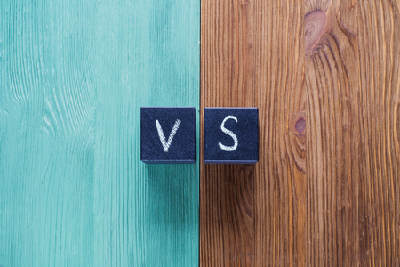 Letters VS on wooden background with copy space. The concept of making choice.  Versus letters. Turquoise and brown wooden background and black cubes with letters VS.の写真素材