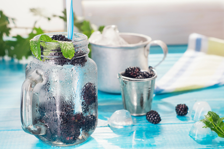 Cold fresh lemonade with blackberry and mint in glass mason jar.  Refreshing blackberry ice cold cocktail on blue table, berries and ice for cocktail preparation. Tasty blackberry drink, mojito.の写真素材