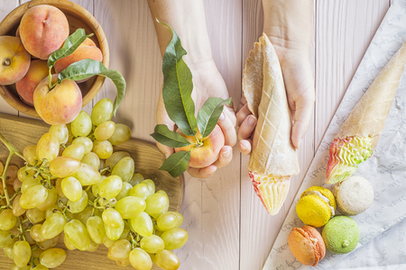 Hands of a young woman holding a cake and peach, making a choice between them. Woman making a choice between sweets and fruits. Healthy vs unhealthy food. top view, flat lay.の写真素材