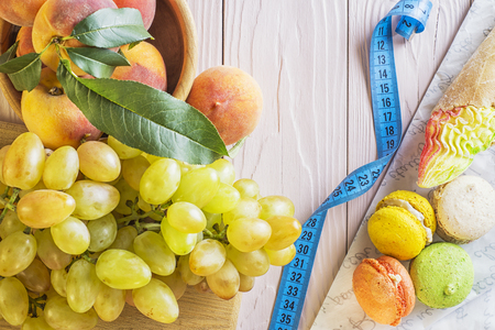 Choosing between Fruits and Sweets. Healthy versus unhealthy food. Weight Loss. Unhealthy tempting cakes and healthy fruits. Healthy and unhealthy food is divided by a measuring tape.の写真素材