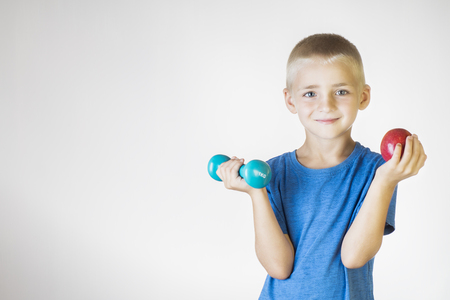Closeup portrait happy, smiling boy, lifting red apple and dumbbell. The concept of healthy lifestyle. Sports and activities for children.の写真素材
