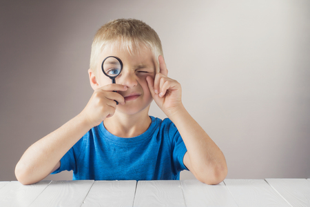 Curious boy with a clever face looks through the magnifying glass and lifts his index finger up. The concept of logical thinking.の写真素材