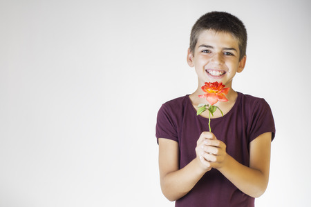 Closeup portrait happy smiling boy with orange rose. Beautiful young boy holding a flower and looking at camera. Mother's day concept.の写真素材