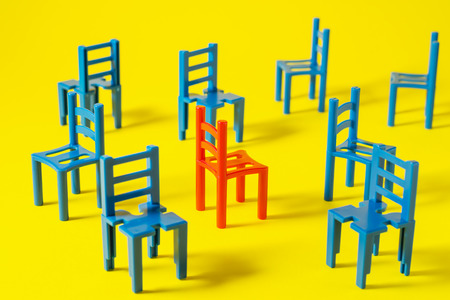 Unique red chair in a group blue others. Leadership concept. Empty chairs  on yellow background. The concept of uniqueness, distinction from others.の写真素材