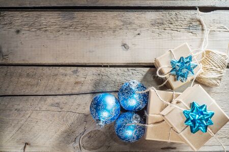 Three craft cardboard gift boxes and blue christmas balls on a rustic wooden background. Gift kraft...