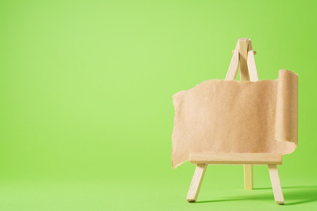 Small easel with blank paper on green background. Torn sheet of paper on easel.  Place for your text.の写真素材
