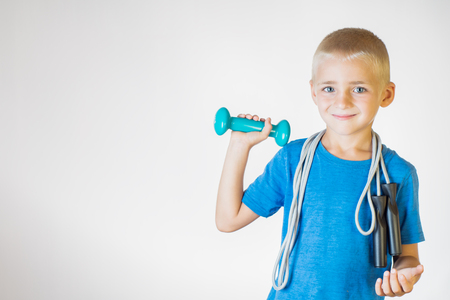 Boy with skipping rope and dumbbell. Portrait happy, smiling boy holding a jump rope and dumbbell. The concept of a healthy lifestyle, sport or workout.の写真素材