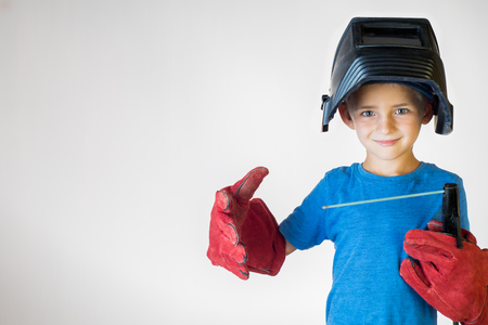 Happy little kid in welder mask and welding equipment. Welding equipment, welding mask, protective leather gloves, welding electrodes. Fun concept. Child dreaming of future profession. Career choice. の写真素材
