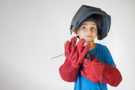 Happy little kid in welder mask and welding equipment. Welding equipment, welding mask, protective leather gloves, welding electrodes. Fun concept. Child dreaming of future profession. Career choice. の写真素材