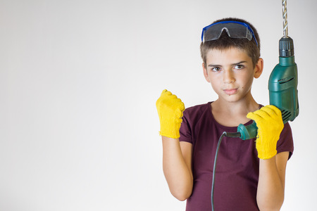 Portrait of young boy holding electric drill. Dreams of future profession. Smiling worker. Cheerful boy using electric drill.の写真素材