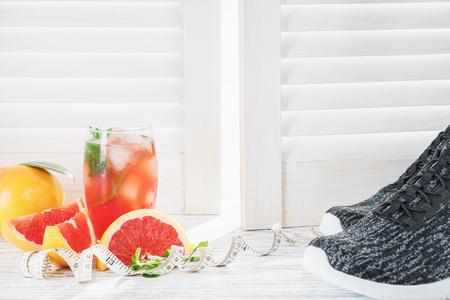 Fresh grapefruits and grapefruit juice, sneakers and measuring tape, on rustic white wooden table opposite the blindsの写真素材