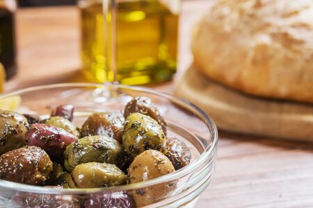 Glass bowl with different kind of olives and fresh bread ciabatta on wooden table.の写真素材