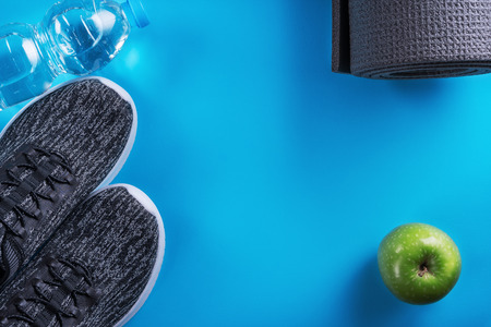 Sport shoes, bottle of water, apple and yoga mat with copy space on blue background.の写真素材